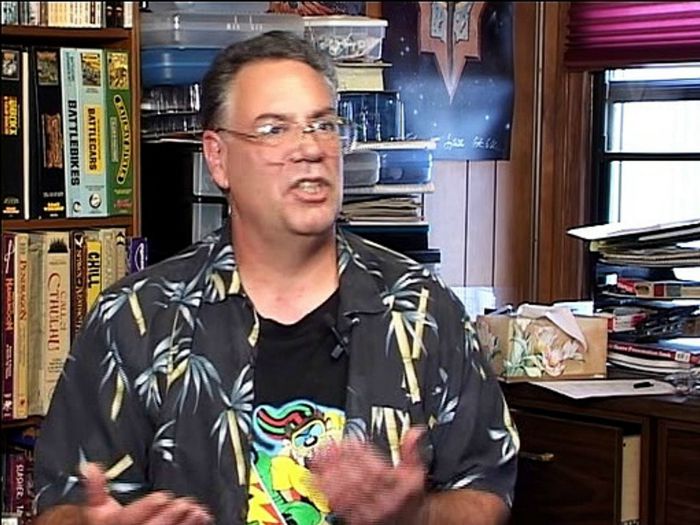 På dette let gnidrede screen grab kan man i baggrunden se DiTillios kærlighed til spil. Her ses bl.a. Battlecars og Battlebikes foruden rollespillet Chill og et stort Call of Cthulhu-boks-sæt.